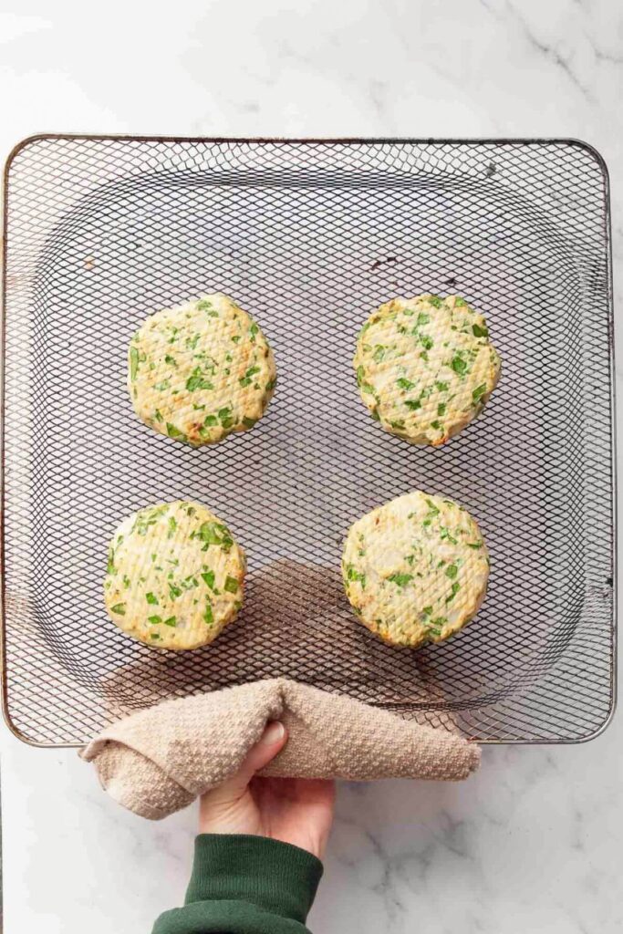four cooked chicken burgers in an air fryer basket