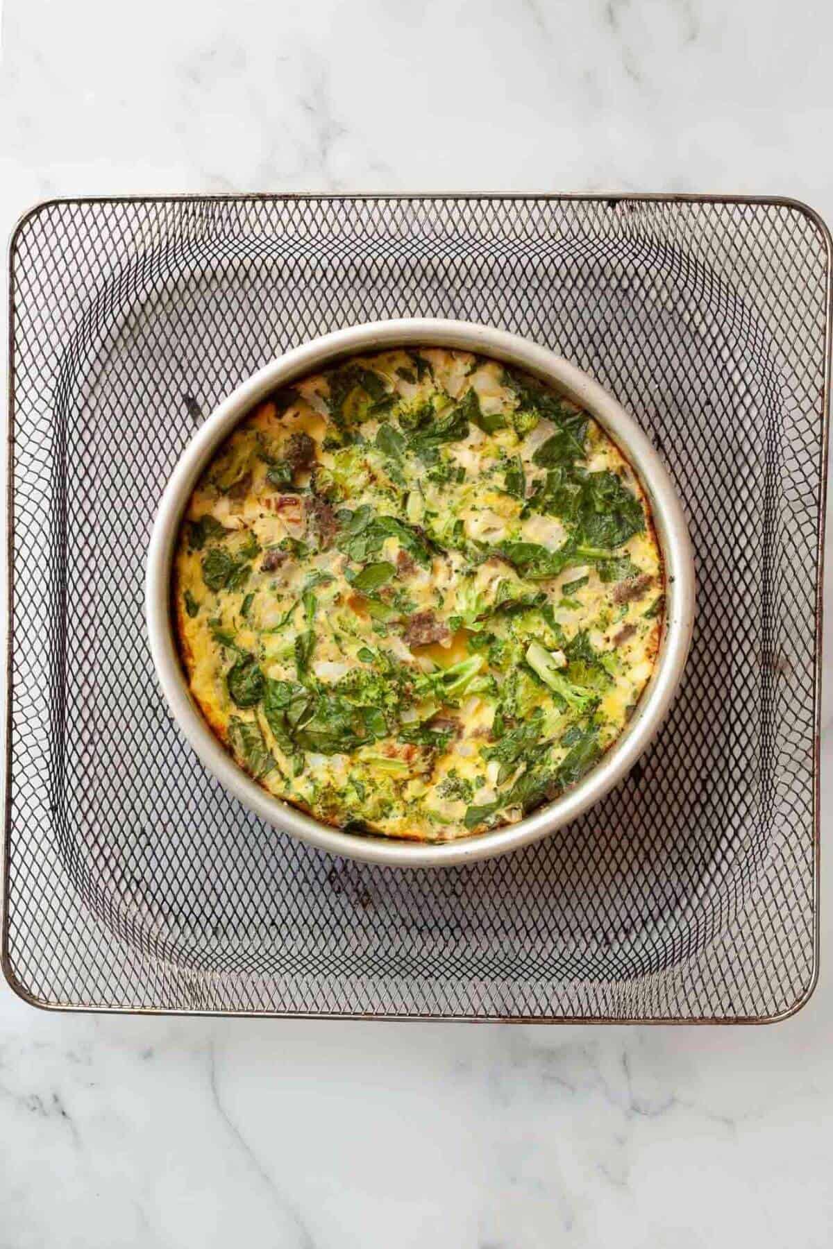 Golden, fully cooked frittata in the air fryer basket with the foil removed.
