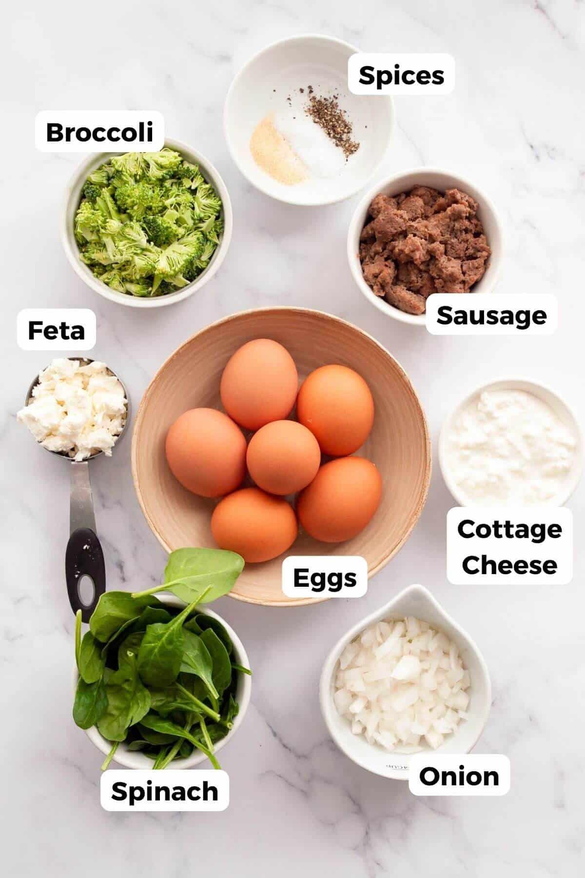 Labeled ingredients for an air fryer frittata: eggs, cottage cheese, broccoli, spinach, onion, chicken sausage, feta, and spices.