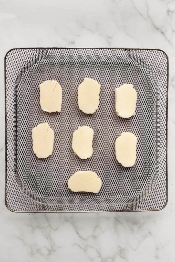 seven pieces of raw halloumi cheese in air fryer basket before cooking