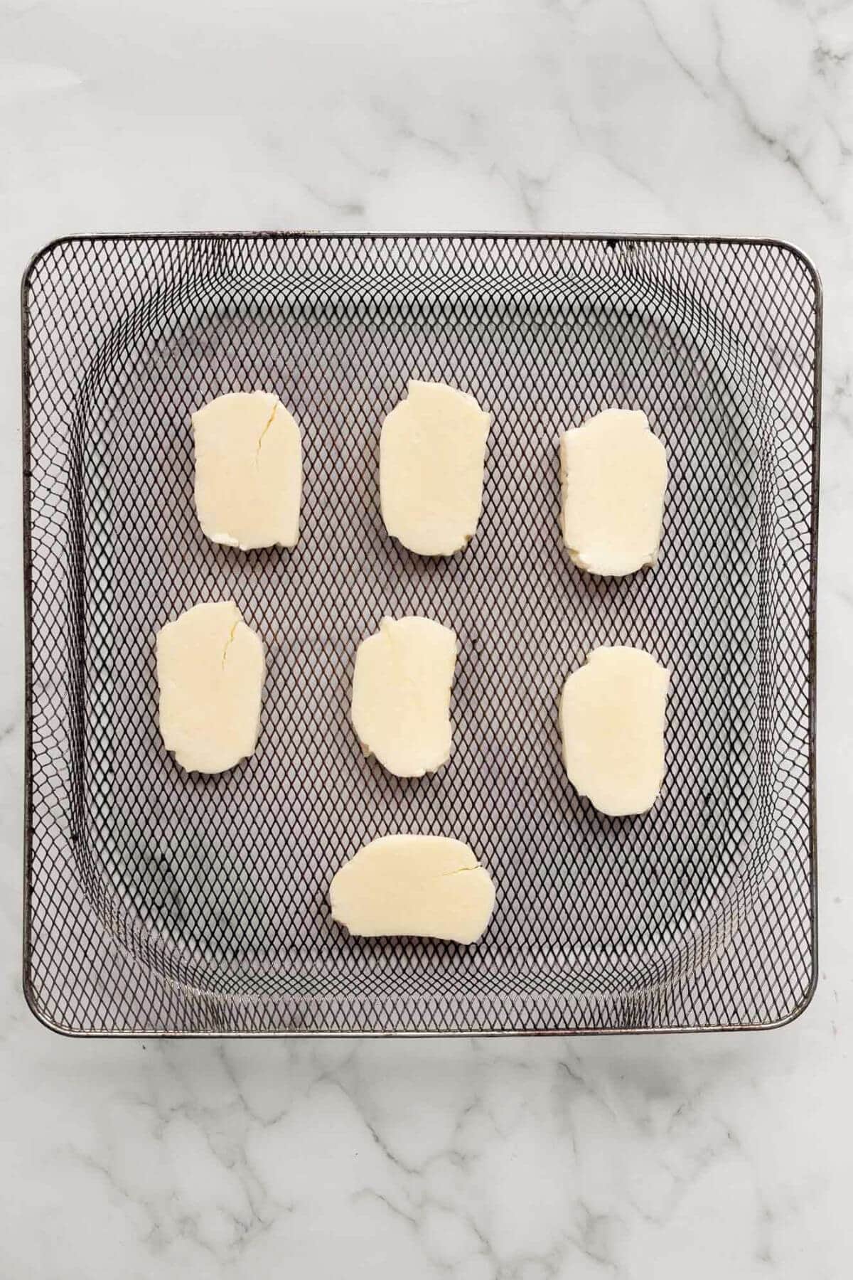 Uncooked halloumi slices spaced evenly in an air fryer basket.