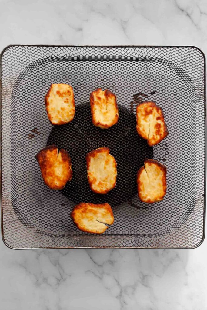 seven pieces of crispy halloumi cheese in air fryer basket after being air fried for 8 minutes