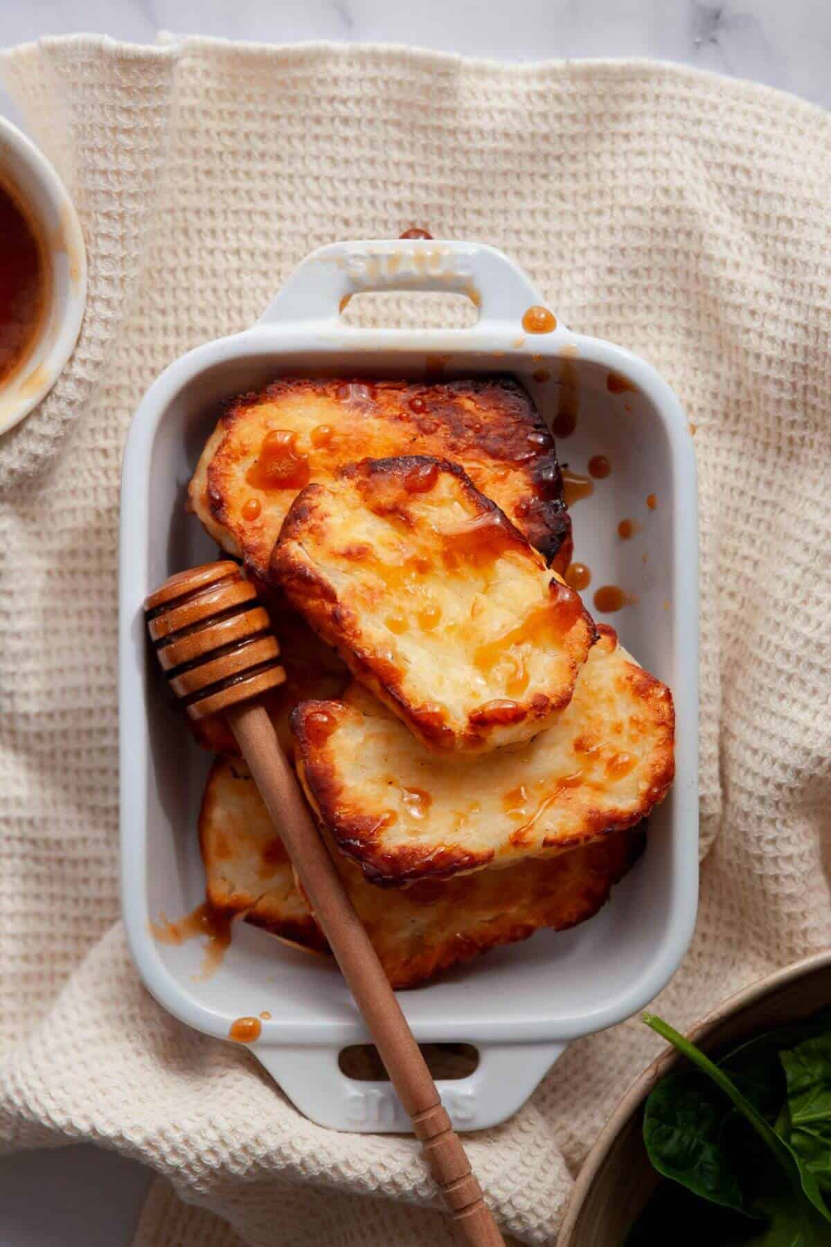 Crispy air fryer halloumi slices in a white dish with honey drizzled over the top.