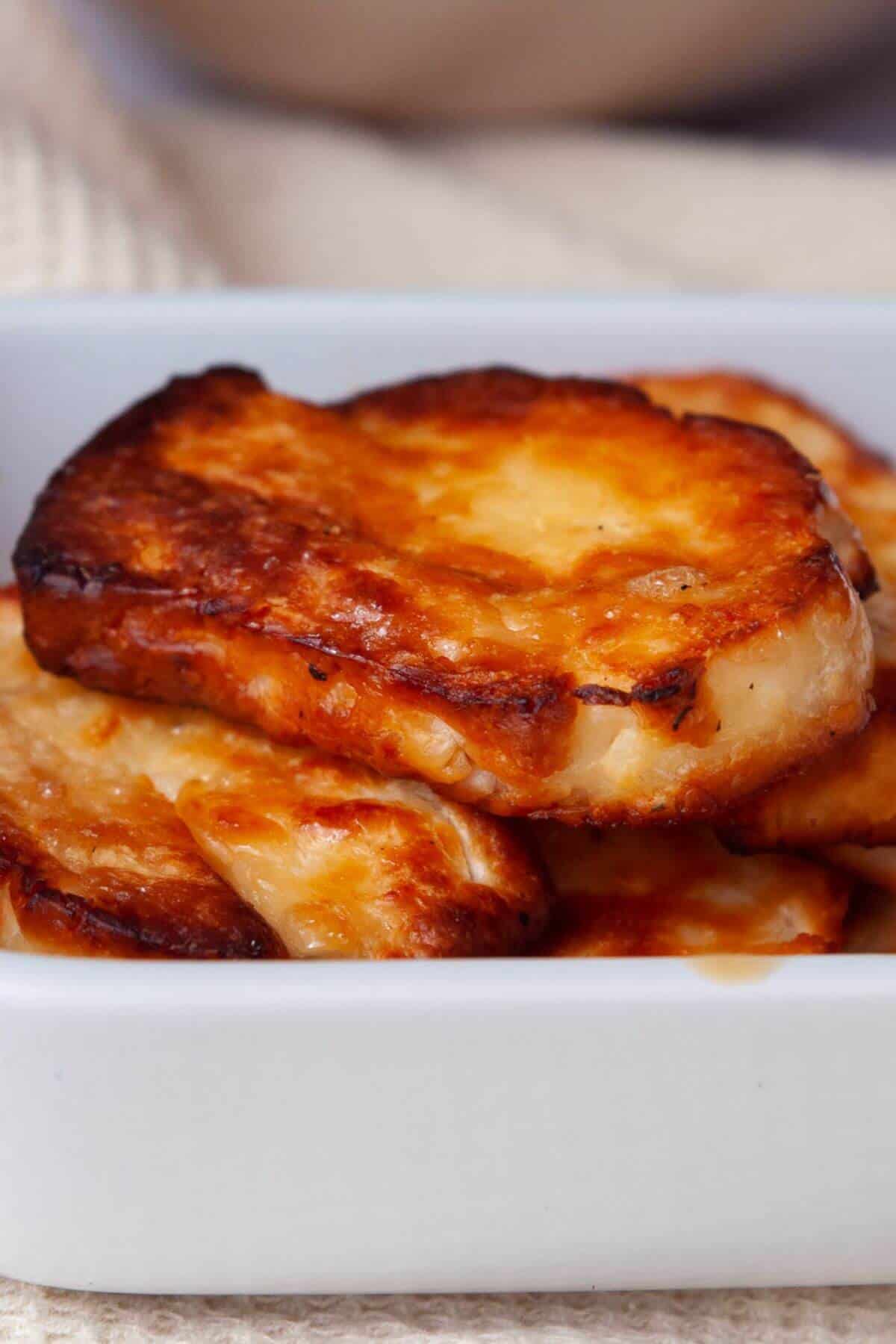 Close up of golden crispy halloumi slices stacked in a white baking dish.