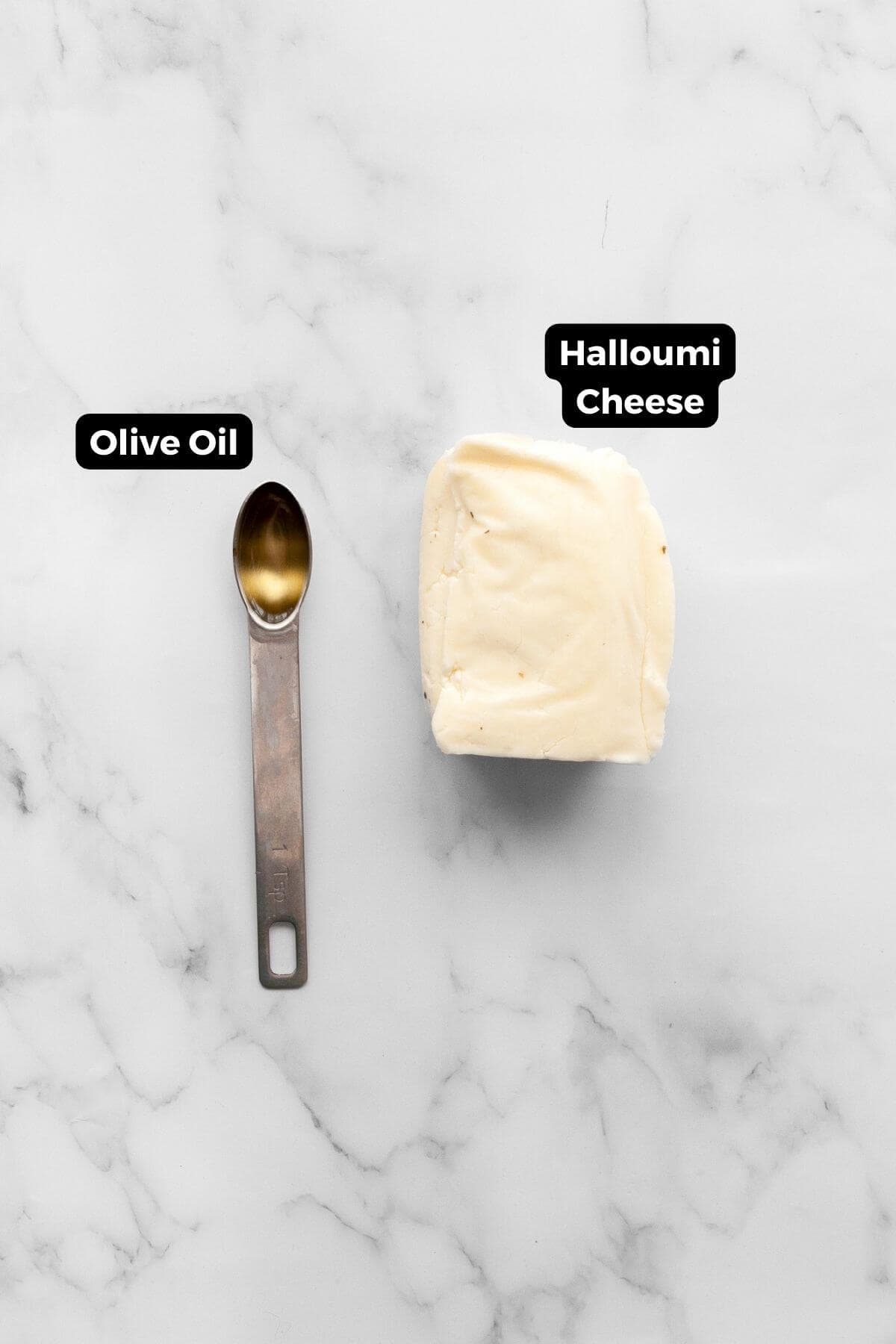 Block of halloumi cheese next to a teaspoon of olive oil on a marble surface.