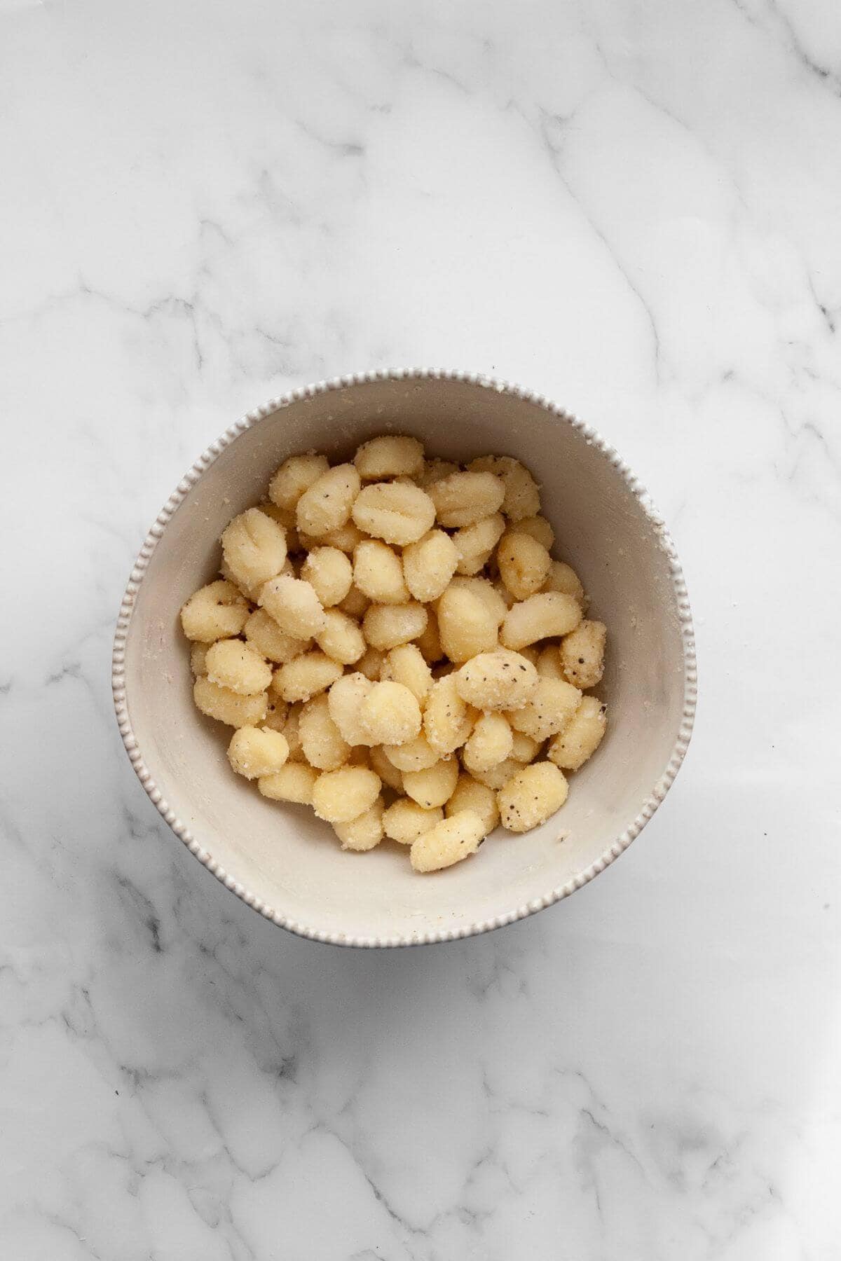 Seasoned un-cooked gnocchi in a mixing bowl.