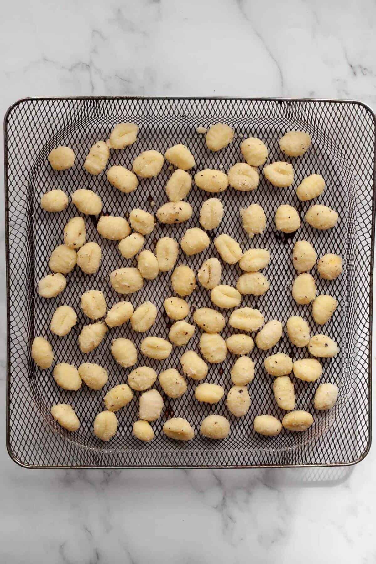 Raw, seasoned gnocchi in air fryer basket before being cooked.
