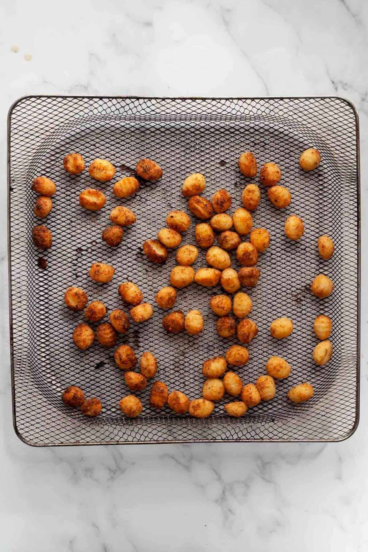 Crispy and gold gnocchi in air fryer basket after being cooked.