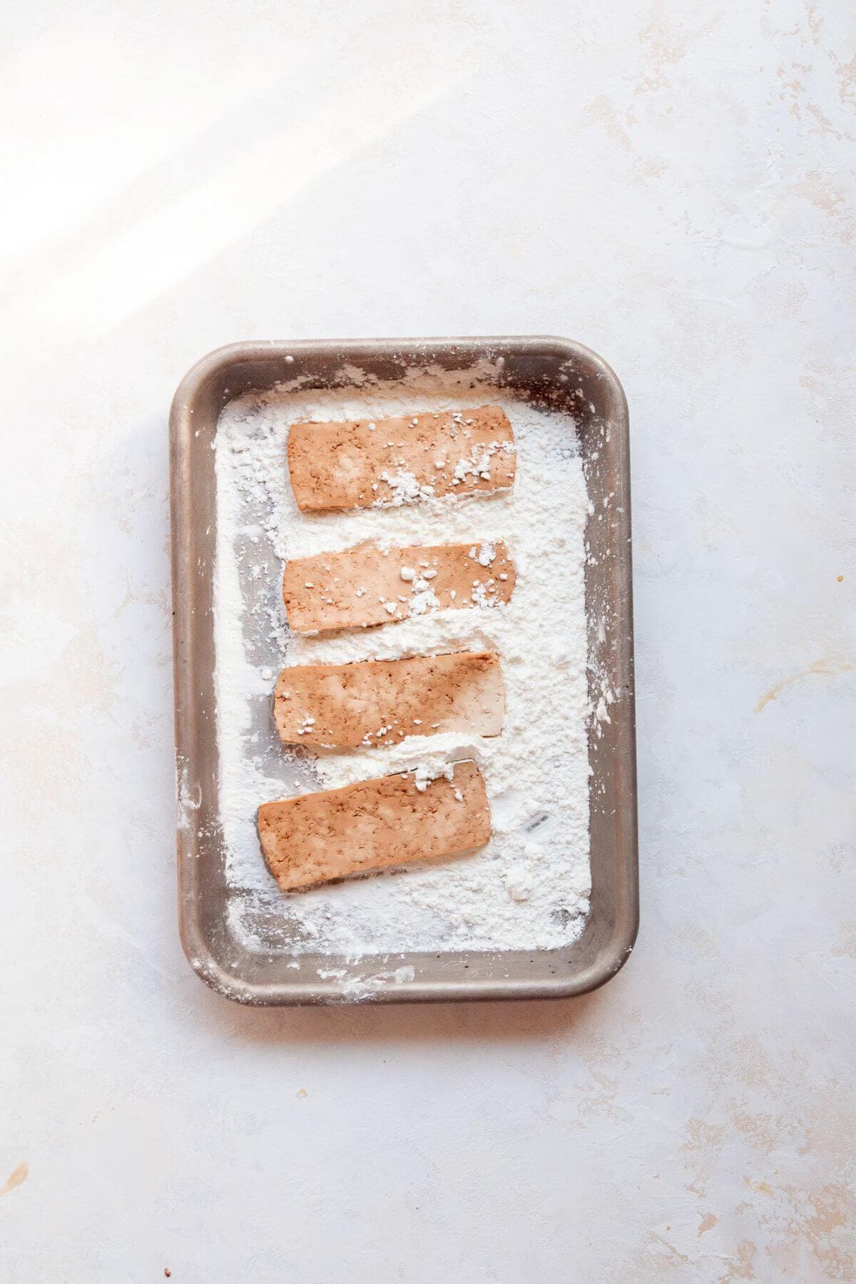 Tofu slices dredged in cornstarch on a sheet pan before breading.