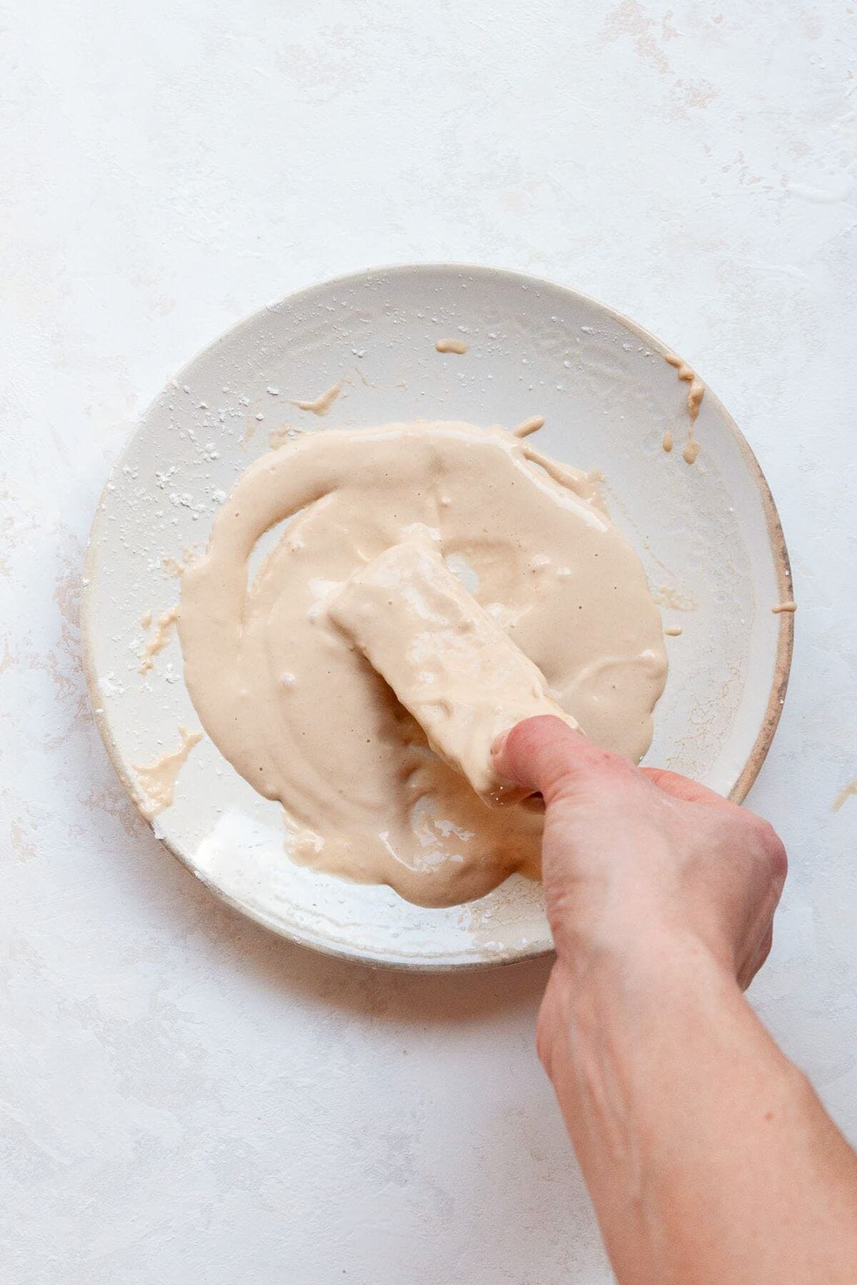 Dipping a tofu slice into the flour batter before coating it in panko.