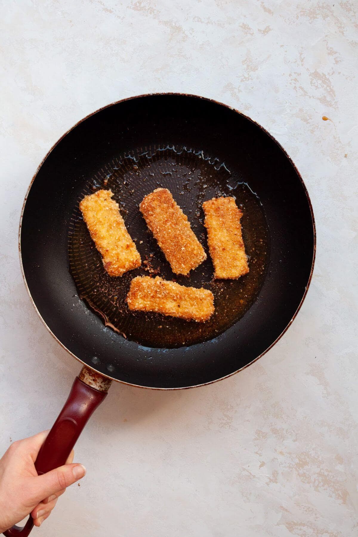 Vegan schnitzel pan frying in olive oil in a black skillet.