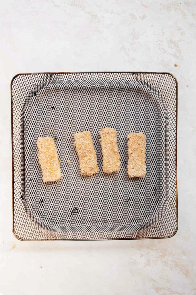 four pieces uncooked breaded tofu schnitzel in air fryer basket before being air fried