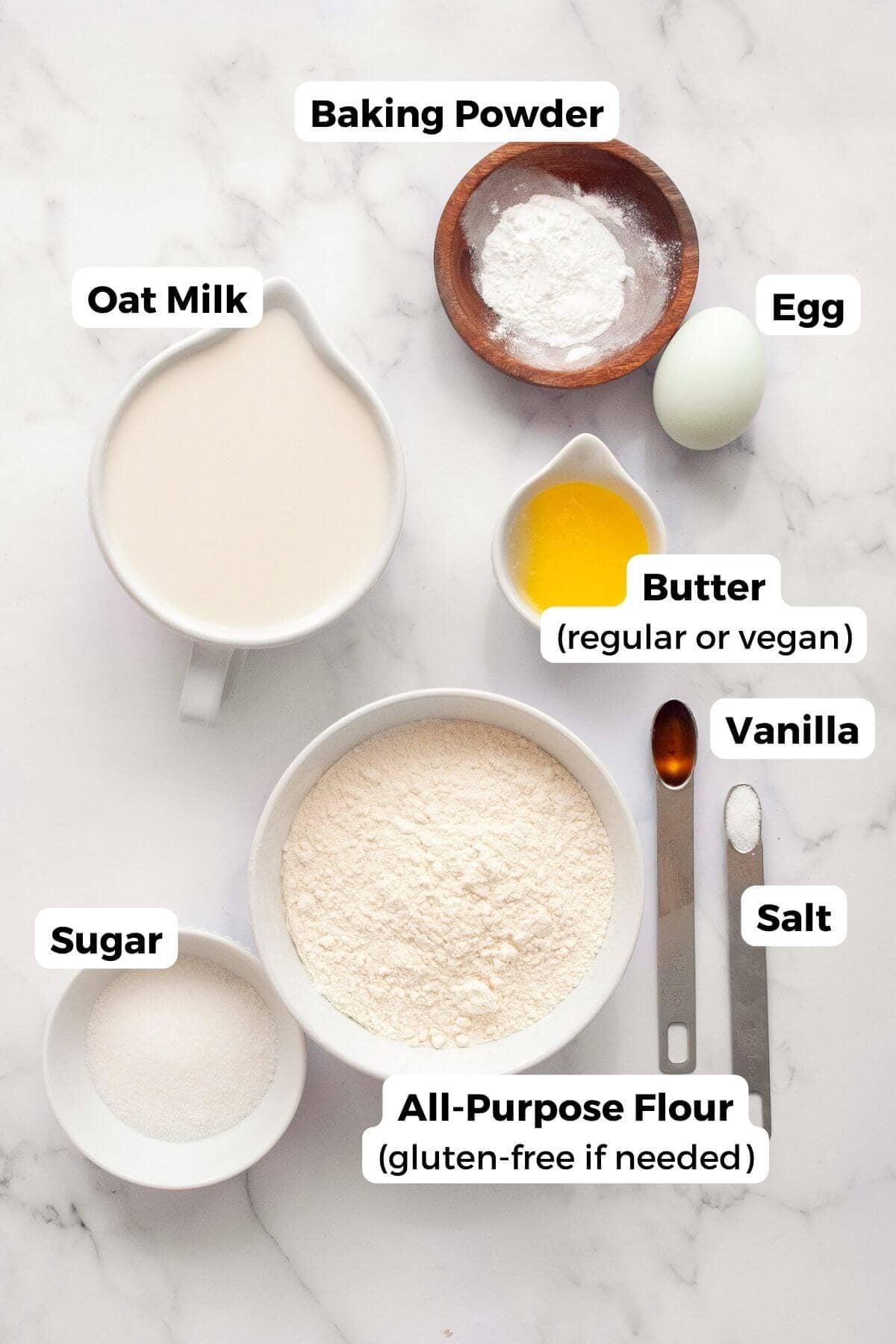 All ingredients in recipe in small bowls with labels, including: flour, oat milk, butter, egg, baking powder, salt, sugar, and vanilla.