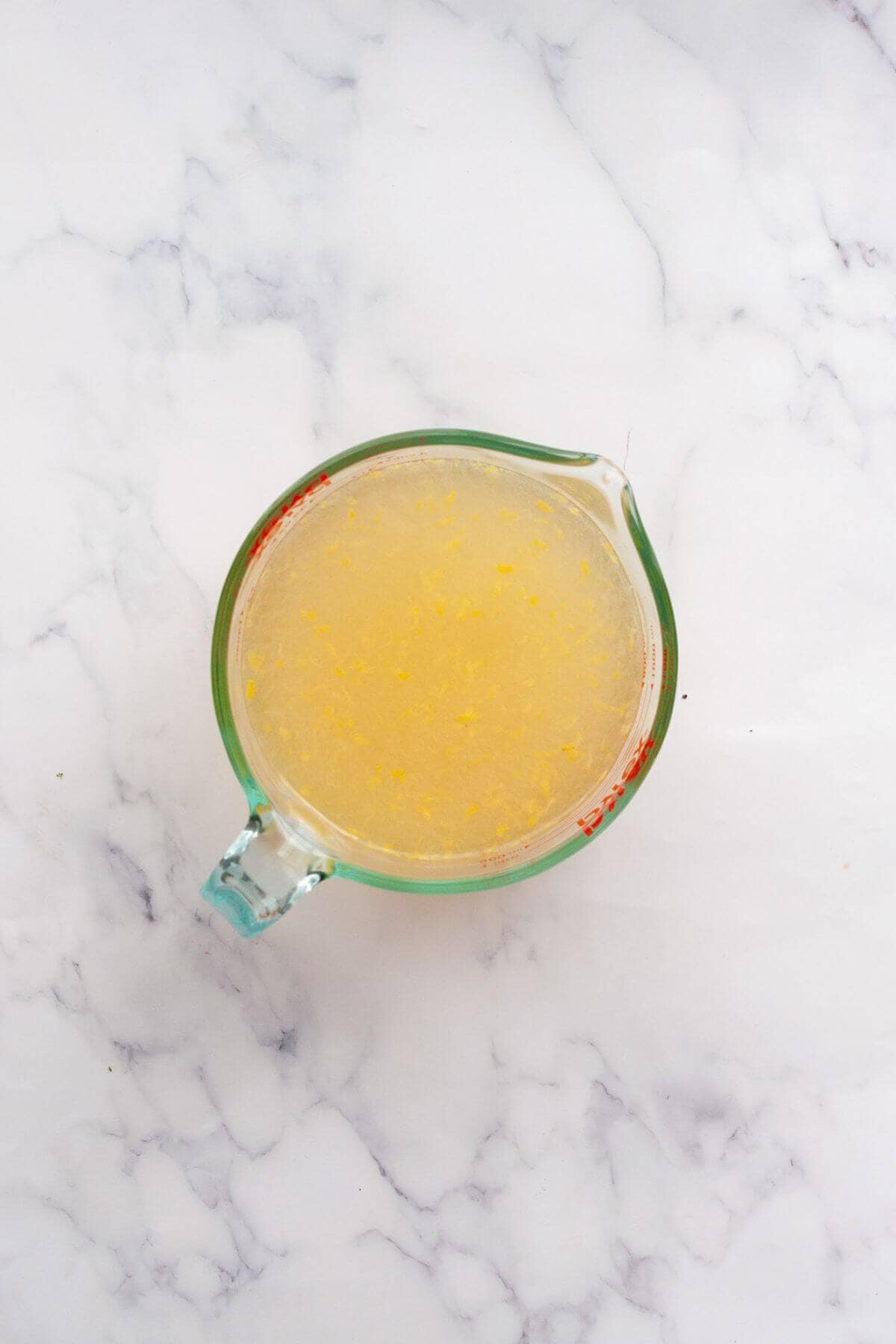 Mixing fresh lemon juice and zest with honey water for homemade lemonade popsicles.