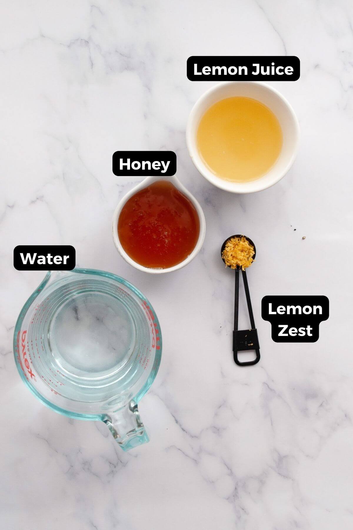 Ingredients for homemade lemonade popsicles: fresh lemon juice, honey, water, and lemon zest in small bowls.