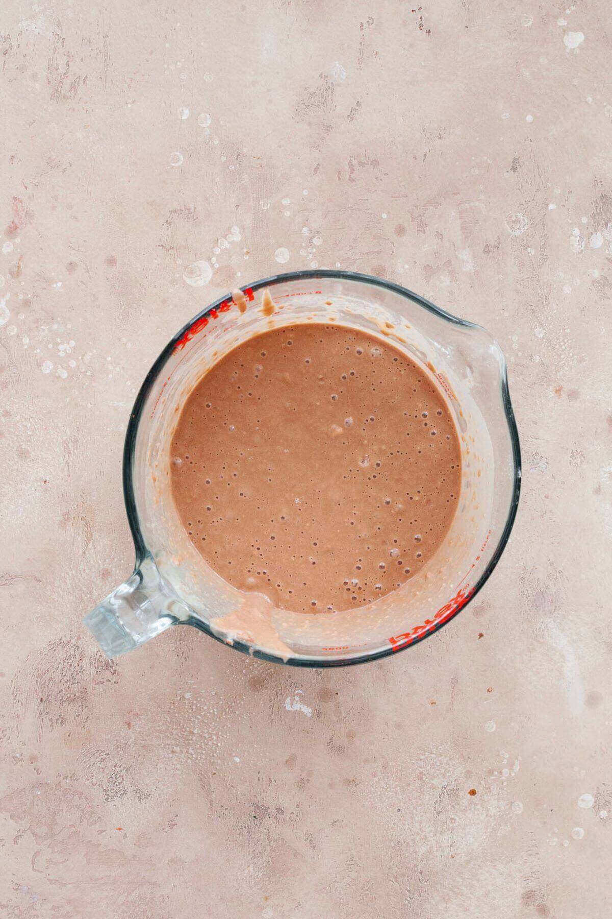 Smooth chocolate Nutella waffle batter in a glass measuring cup.