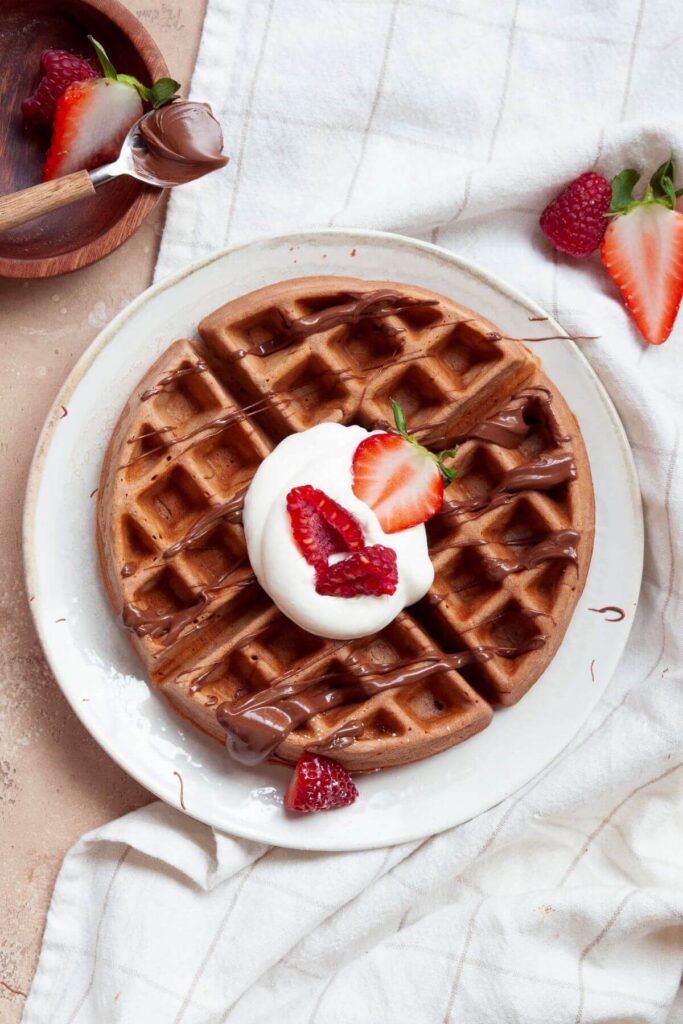 Nutella waffle on a plate with yogurt, strawberries, and raspberries