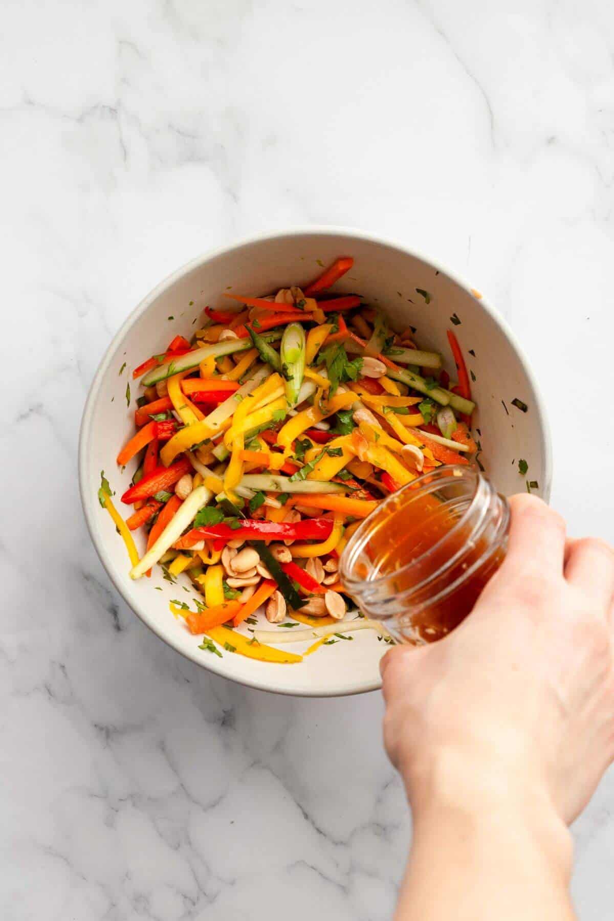 Pouring lime soy dressing over Thai mango salad with fresh vegetables in a large bowl
.