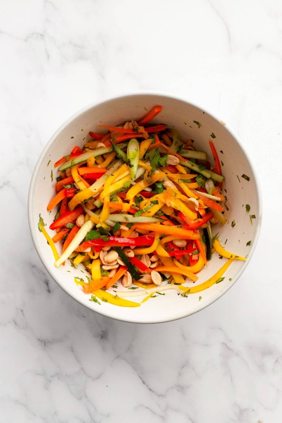 Mango, cucumber, bell pepper, carrot, herbs, and peanuts in a large bowl.