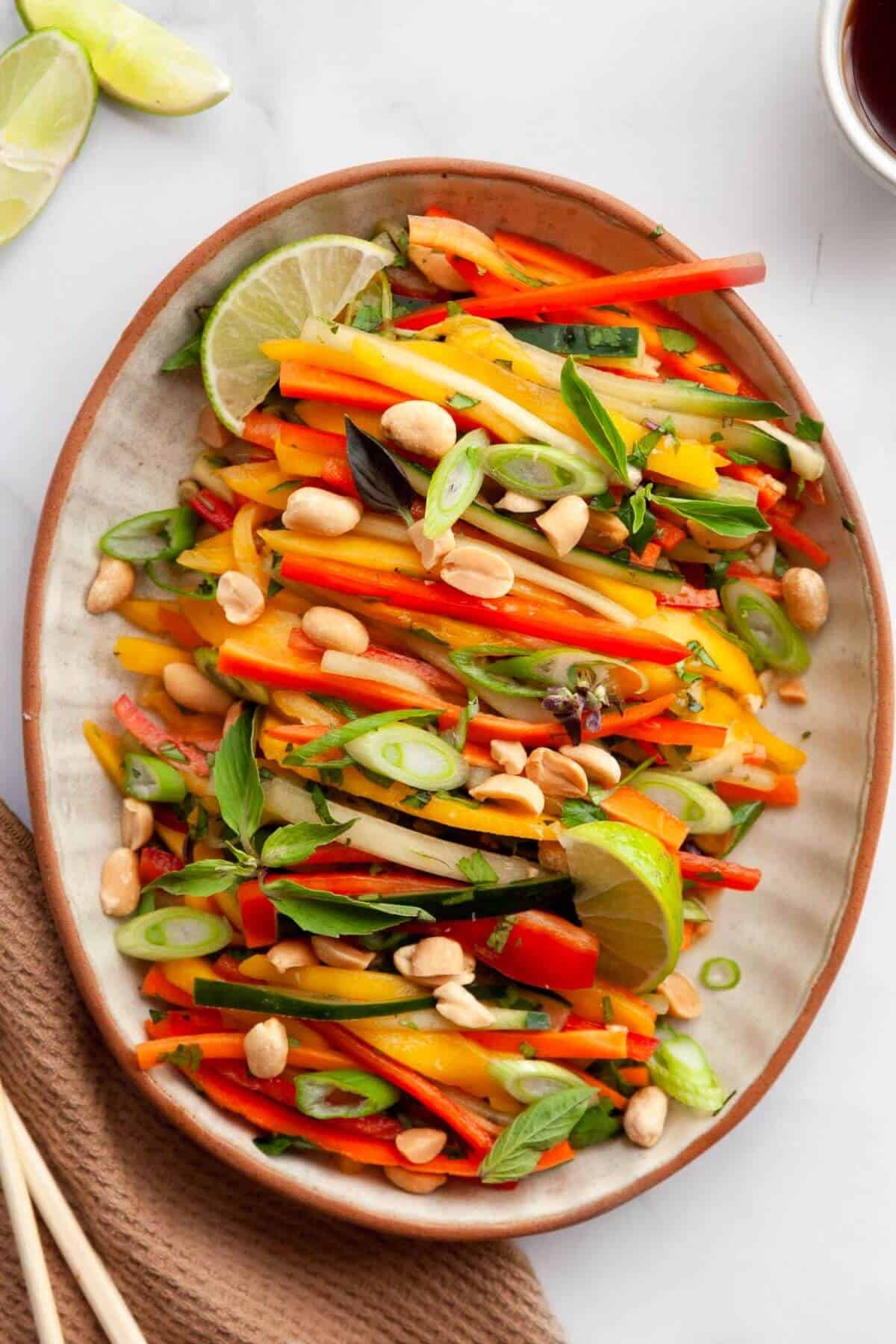 Thai mango salad topped with roasted peanuts, fresh Thai basil, and a lime wedge ready to serve.