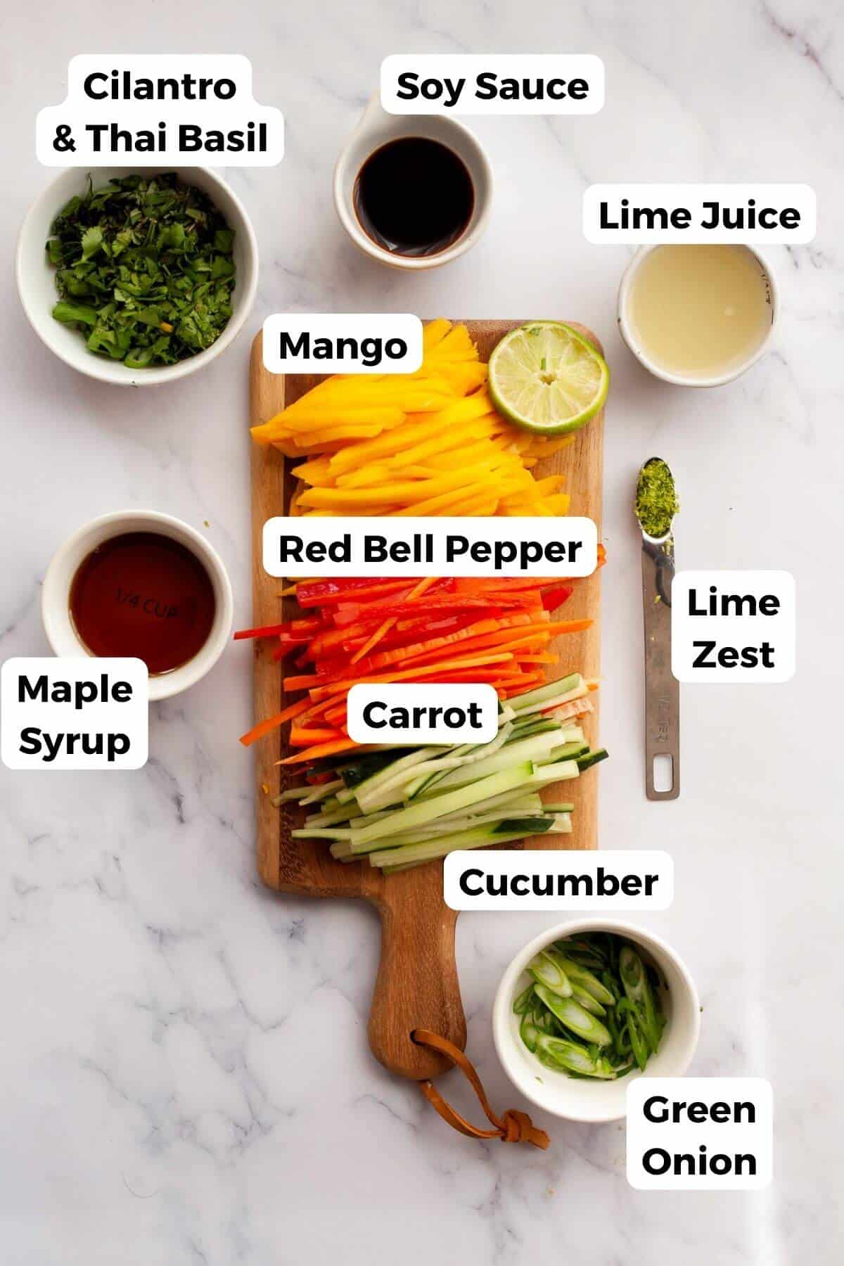 Ingredients for Thai mango salad including mango, red bell pepper, carrot, cucumber, green onion, cilantro, Thai basil, soy sauce, lime juice, lime zest, and maple syrup.