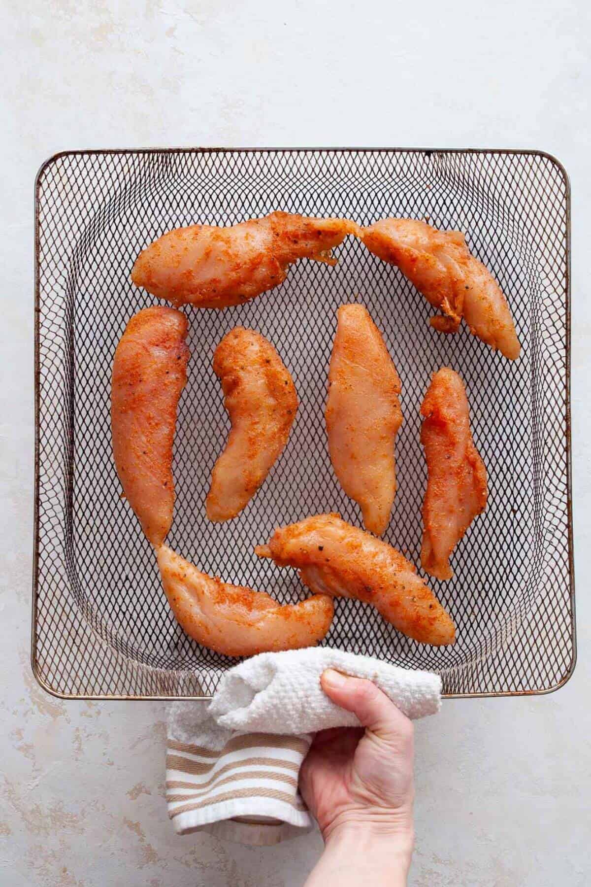 Seasoned chicken tenders arranged in a single layer in an air fryer basket.