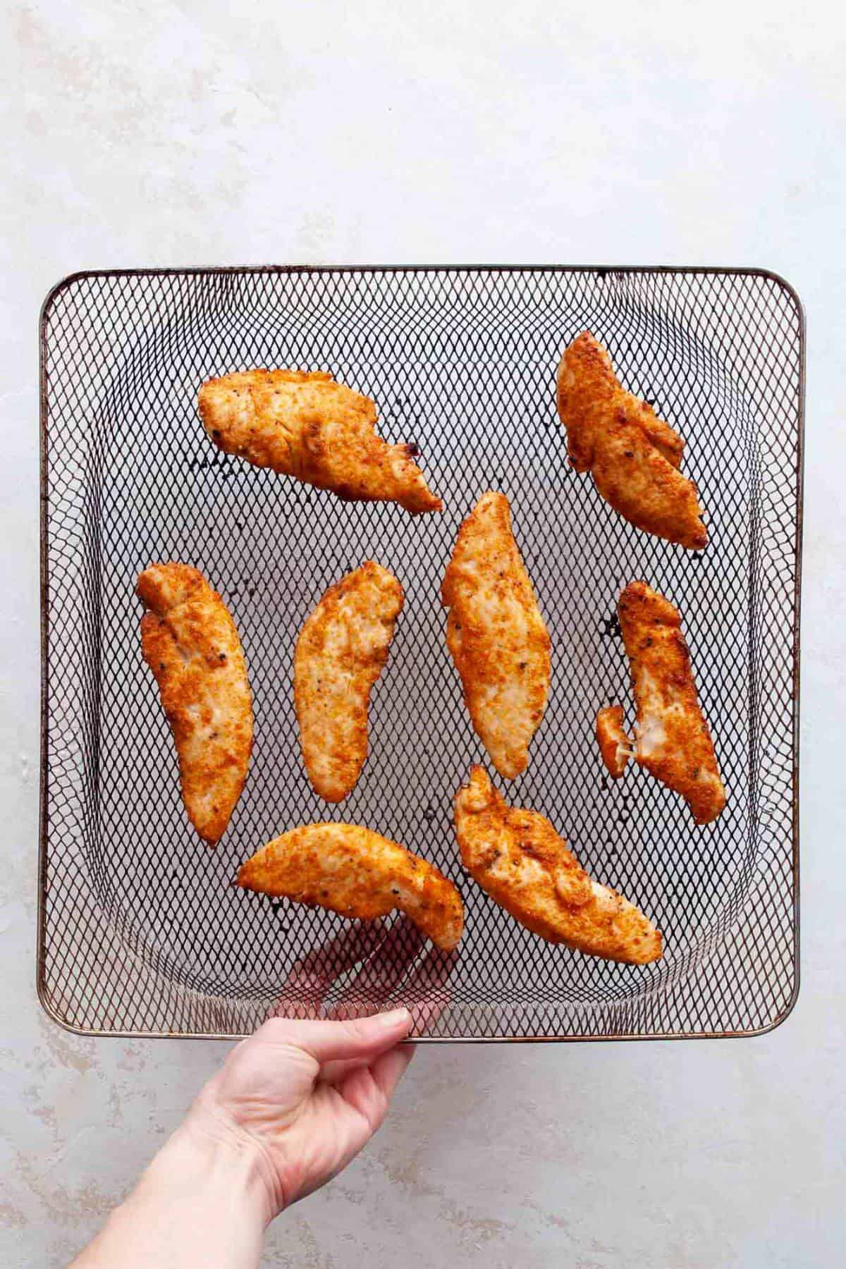Golden air fryer chicken tenders without breading being flipped halfway through cooking.