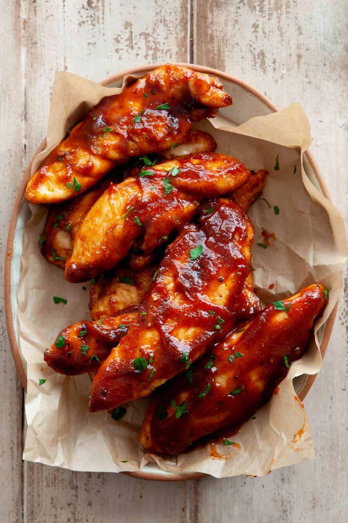 Air fryer chicken tenders tossed in BBQ sauce after cooking, garnished with parsley.
