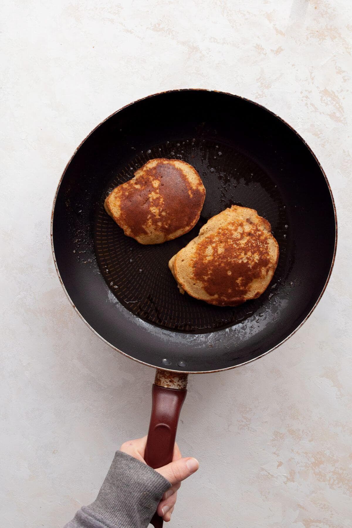 Fluffy almond flour banana pancakes cooking in a pan after being flipped, showing golden brown edges.