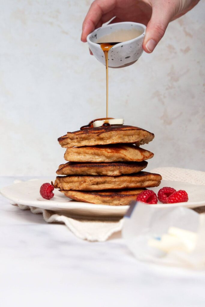 pouring syrup on top of a stack of almond flour banana protein pancakes
