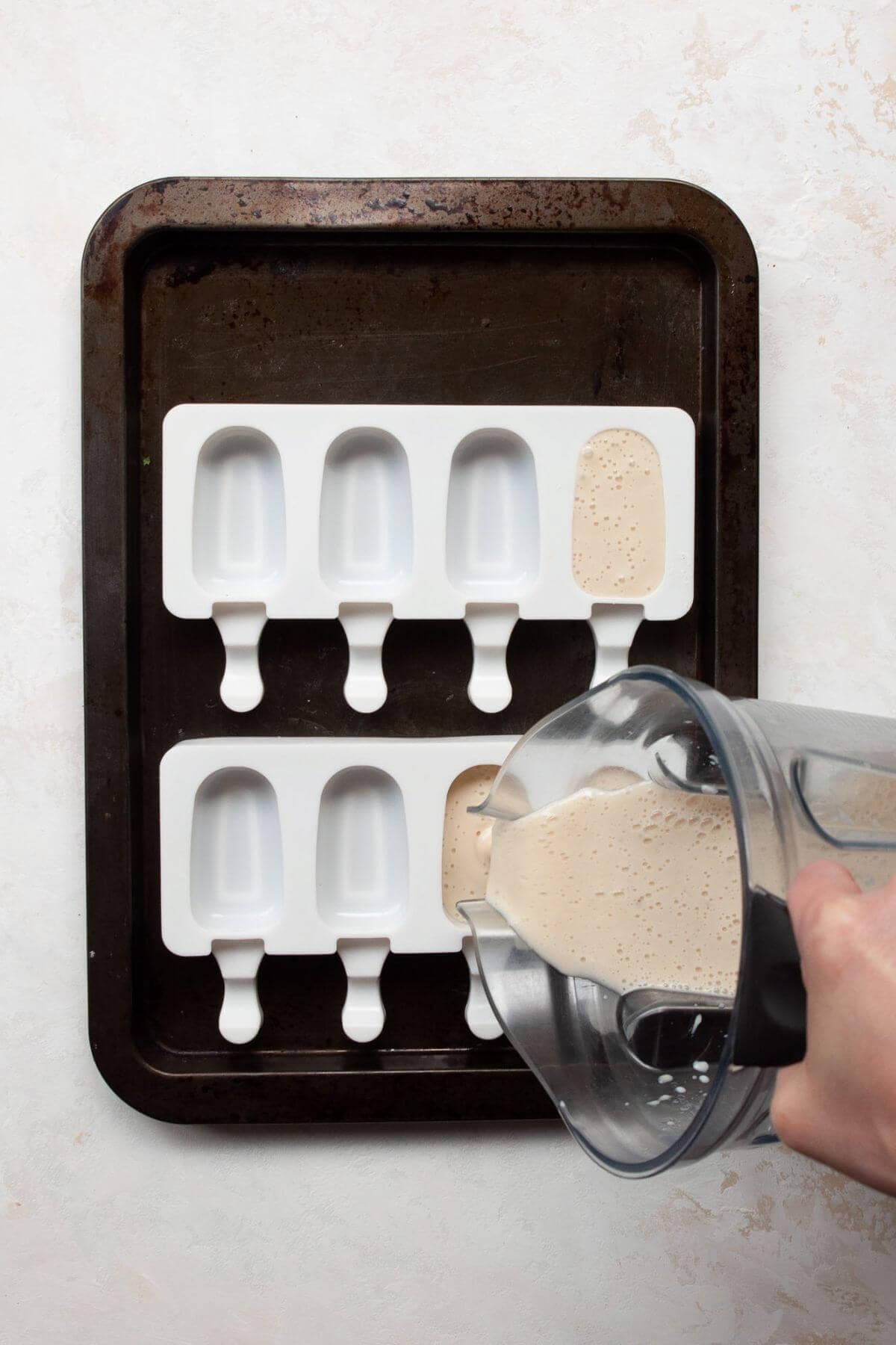 Pouring smooth banana popsicle mixture from a blender into popsicle molds.