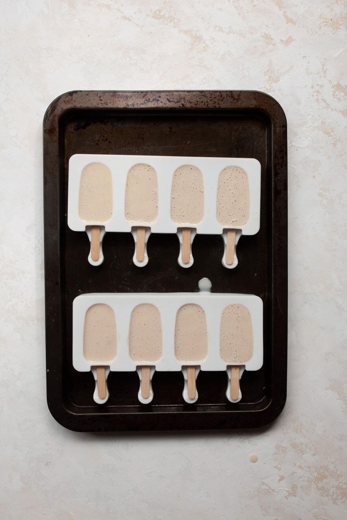 Unfrozen banana popsicles filled in molds, ready to freeze.