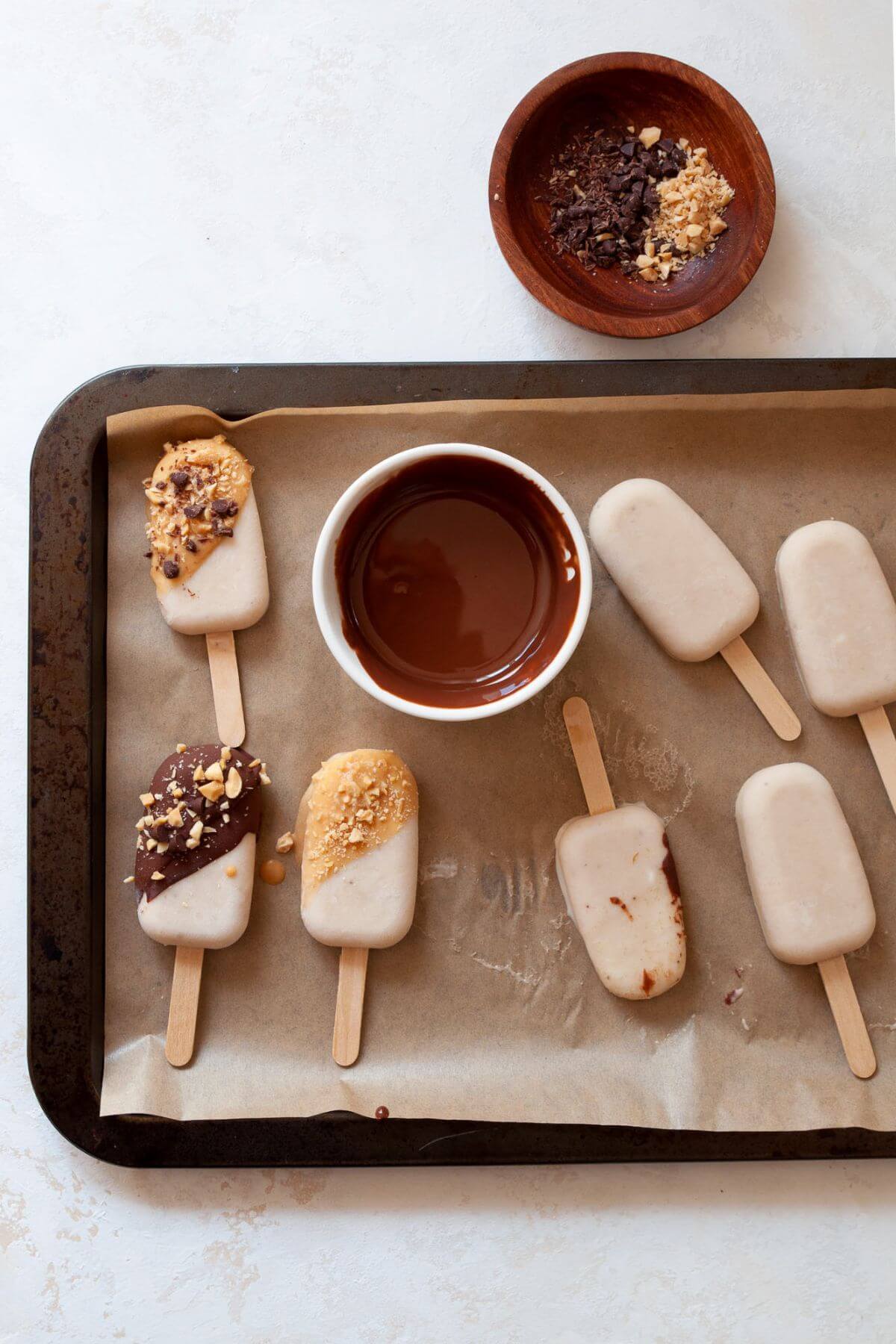 Banana popsicles being dipped and decorated with chocolate and peanut butter magic shells