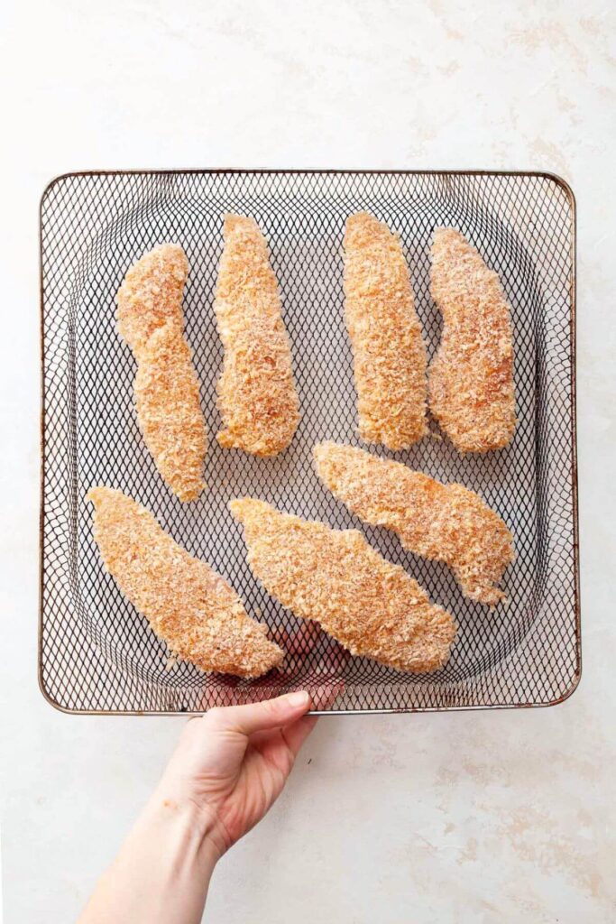 uncooked chicken tenders in an air fryer basket