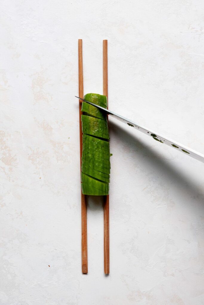 cutting a mini cucumber at a 45-degree angle between two chopsticks
