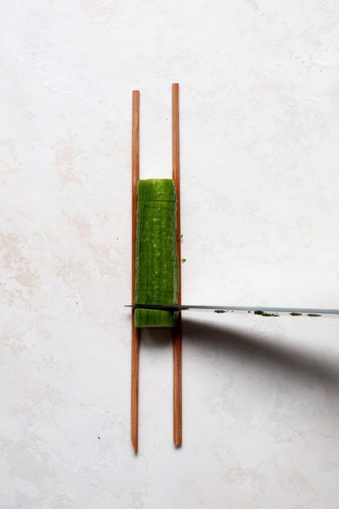 cutting a mini cucumber at a 90-degree angle between two chopsticks