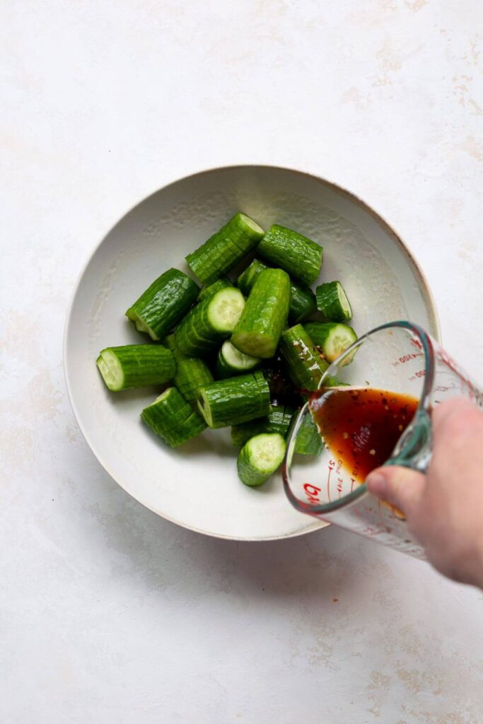 pouring spicy soy dressing on top of accordion cucumbers