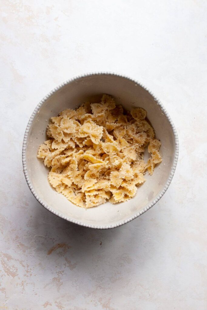 cooked pasta in a mixing bowl with parmesan, olive oil, and seasonings