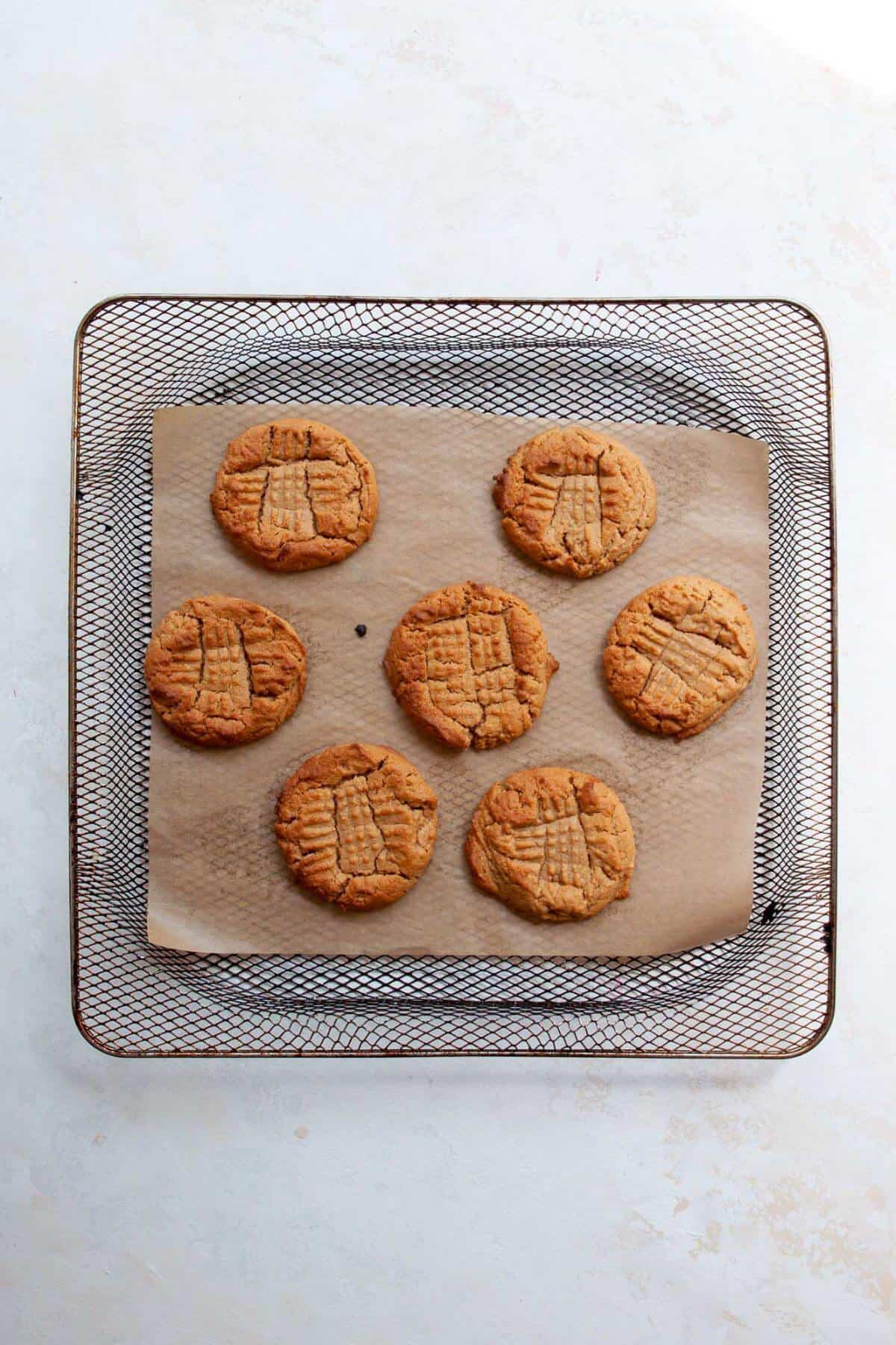 Golden baked air fryer peanut butter cookies resting in the air fryer basket.