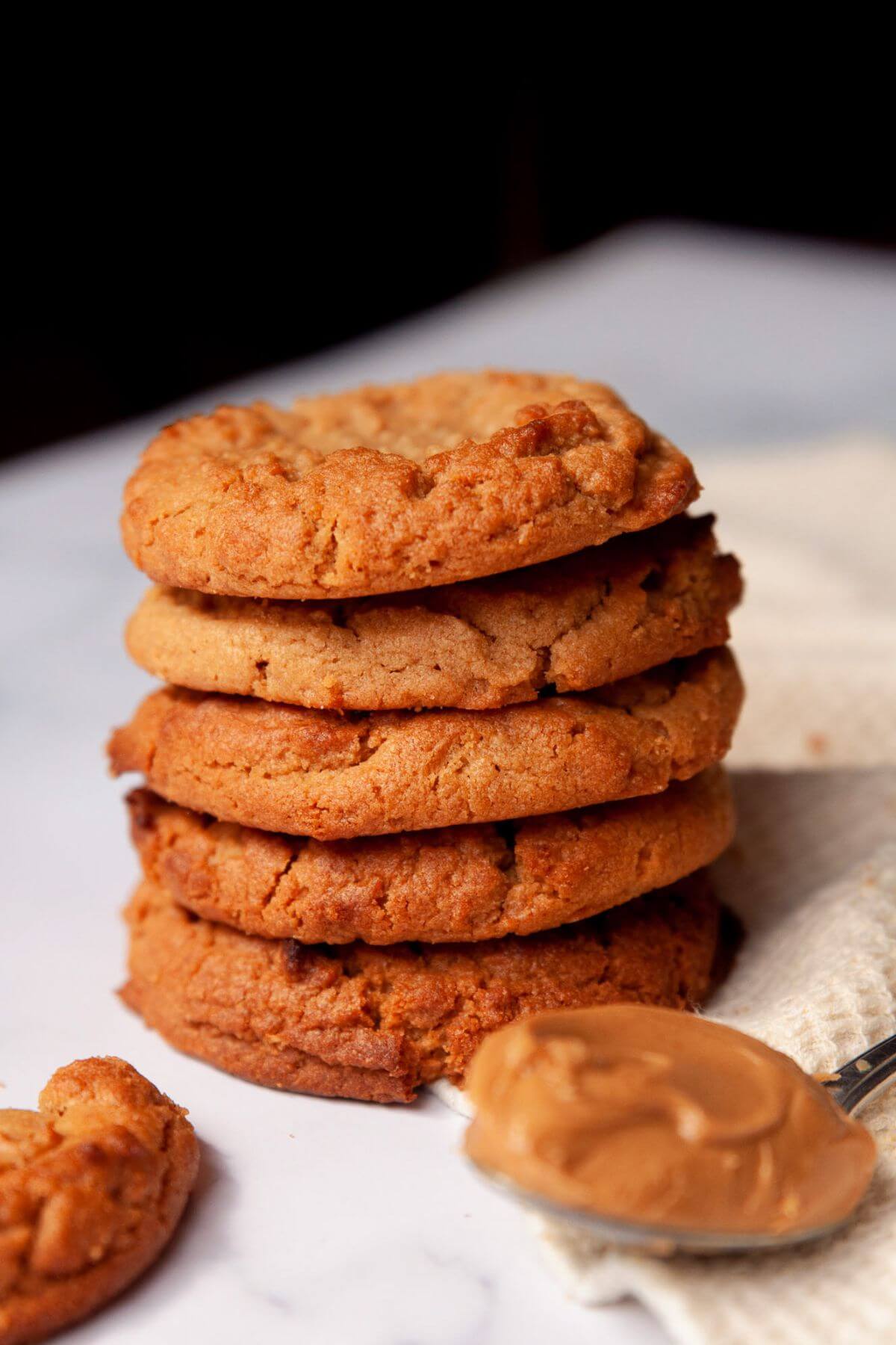Stack of air fryer peanut butter cookies next to a spoonful of creamy peanut butter.