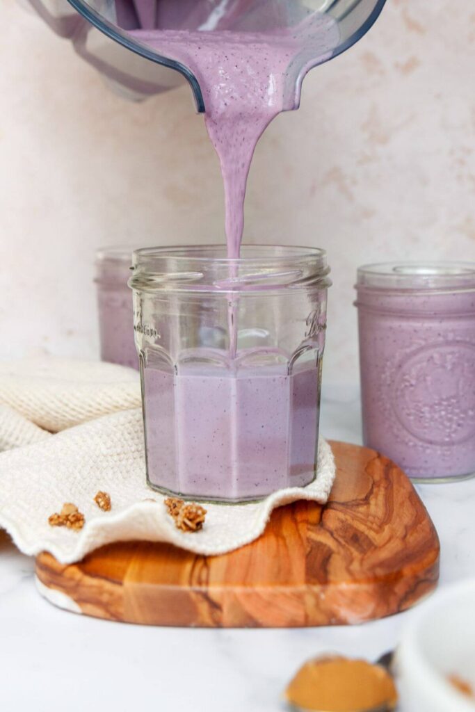pouring blueberry banana protein smoothie into a mason jar