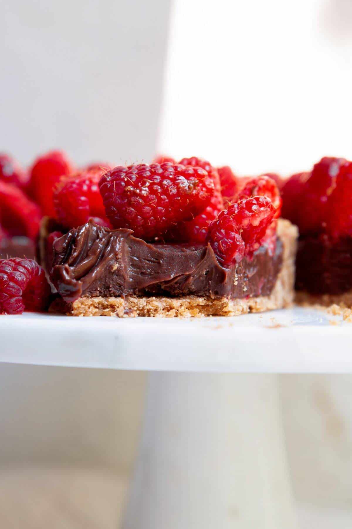 Slice of dark chocolate raspberry tart showing layers of graham cracker crust, chocolate ganache, and fresh raspberries.