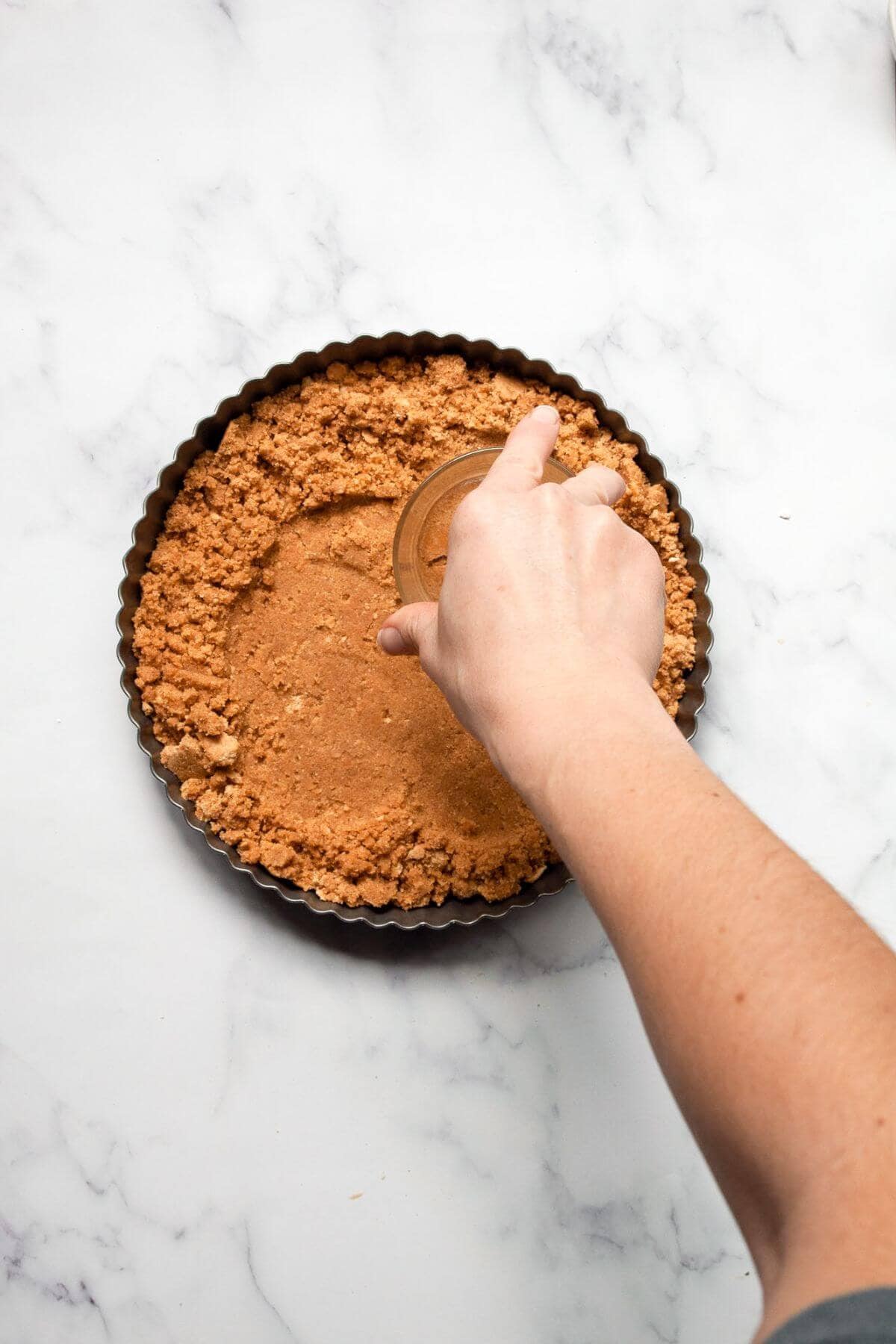 Hand pressing graham cracker crust mixture into an 8-inch fluted tart pan.