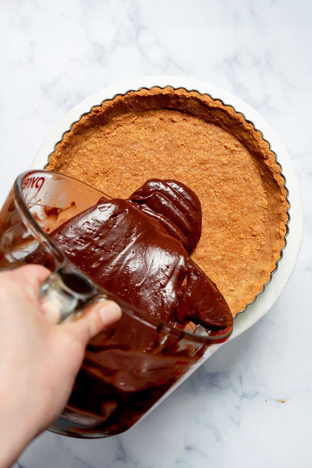 Silky dark chocolate ganache being poured into a pre-baked graham cracker tart crust.