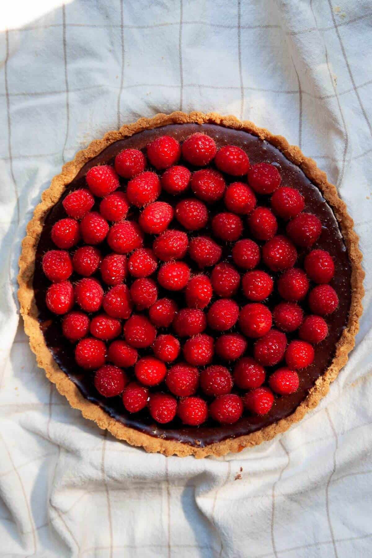 Fresh raspberries arranged in concentric circles on top of a set chocolate ganache tart.