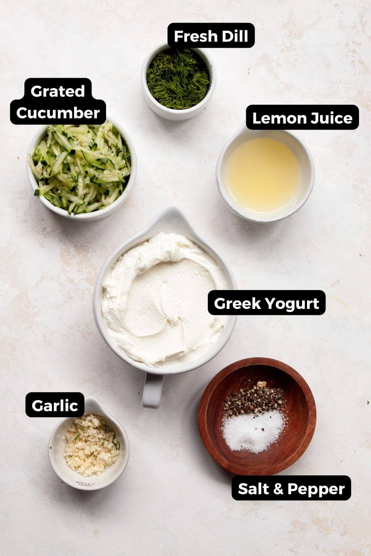 Grated cucumber, Greek yogurt, lemon juice, garlic, dill, salt and pepper in bowls.
