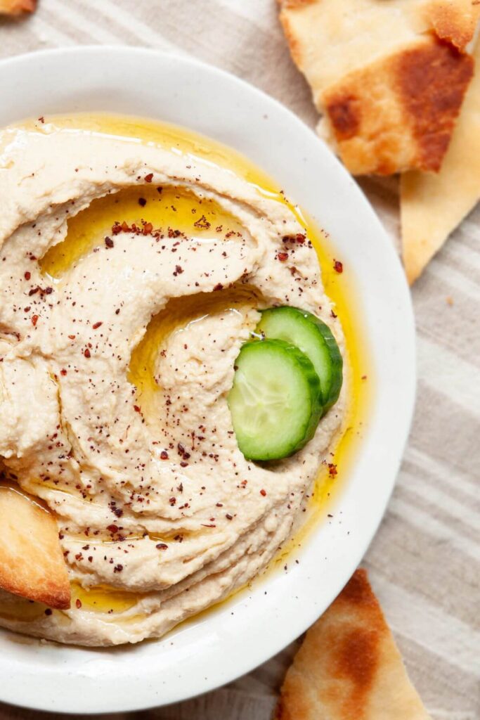homemade blender hummus in a bowl with cucumber rounds