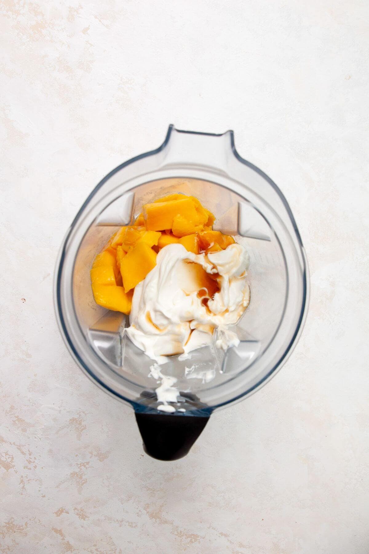 Fresh mango, Greek yogurt, and maple syrup blended together in a clear blender jar.
