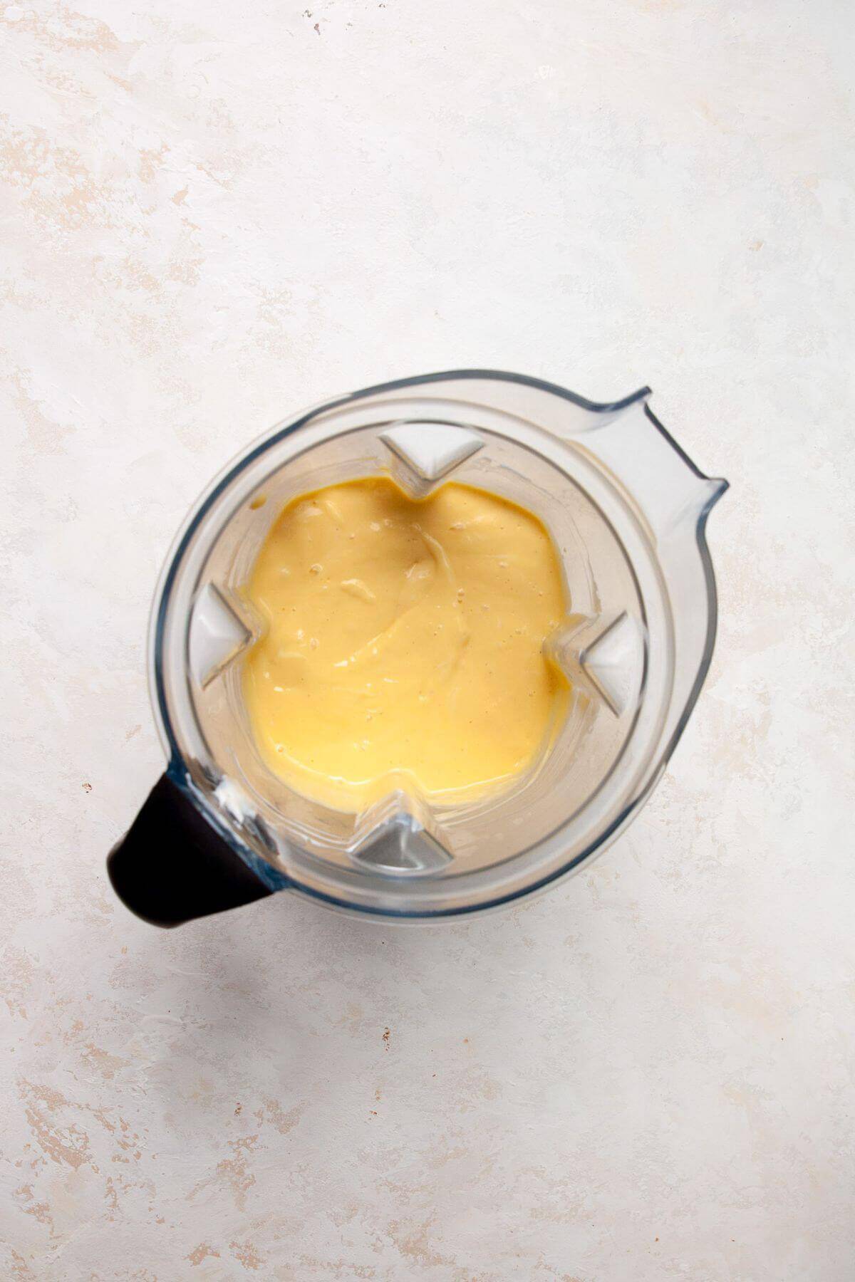 Smooth mango and yogurt mixture blended in a blender, ready to be poured into popsicle molds.