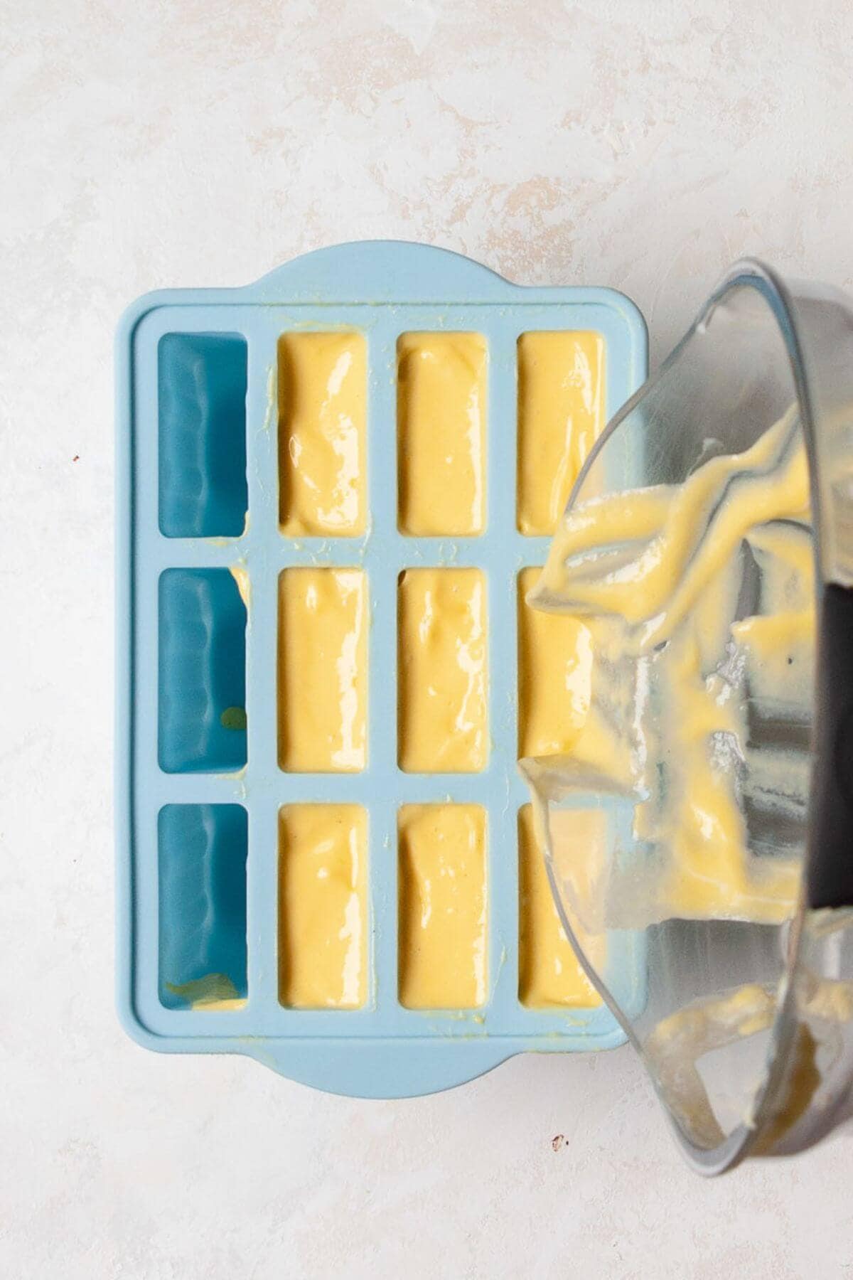 Pouring creamy mango smoothie into popsicle molds before freezing.